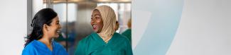 Two young hospital workers in scrubs talk as they exit an elevator. 