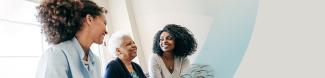 An older woman sits between two younger women in front of a window. All are smiling.